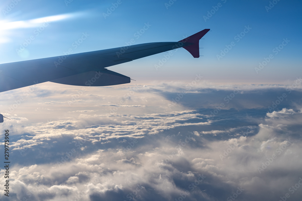 Up in the air, view of aircraft wing silhouette with dark blue sky horizon and cloud background in sun rise time, viewed from airplane window