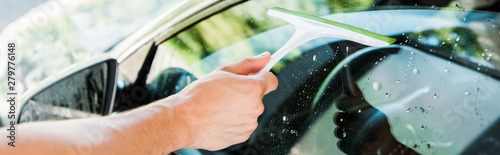 panoramic shot of man holding squeegee while cleaning car window