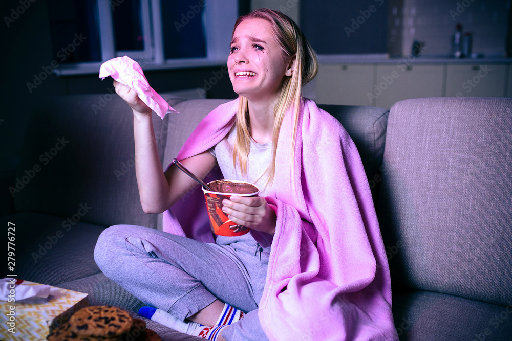 Young woman watching movie at night. Emotional model sitting on sofa and crying. Watching sad