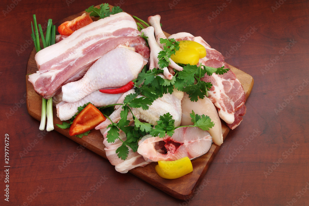 Assortment of meat, chicken and fish with vegetables and greens on wooden board on brown table