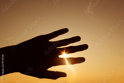 Silhouette of hands against the sunset. Sun with rays between fingers. Minimalism, space for text, warm colors.