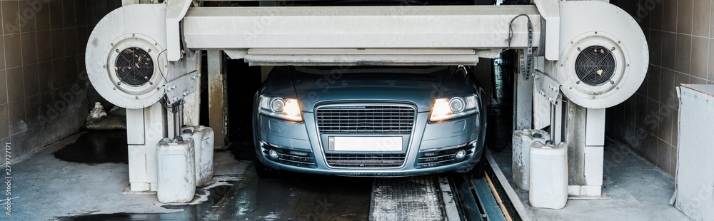 panoramic shot of grey automobile with car headlights shining in car wash service