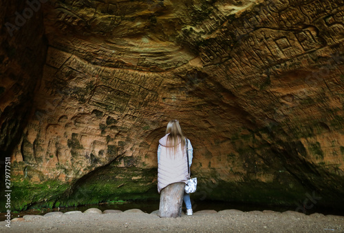 The girl sitting and looking at old sand cave engravings in Sigulda, Latvia. © Liene