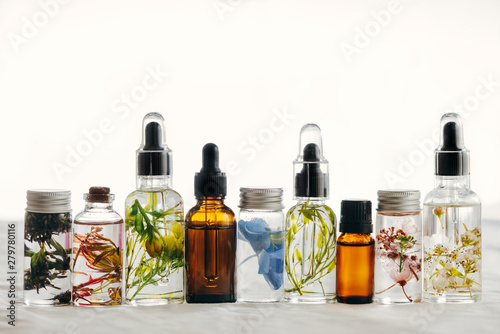 Transparent Bottles of essential oil with fresh herbs.