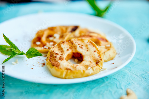 Grilled apples with cinamon on white plate on blue background.