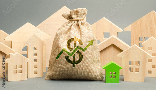 Money bag with arrow up and miniature wooden houses. The concept of rising property prices. High mortgage rates. Expensive rental apartment. Growing demand for home purchase. Real estate market.