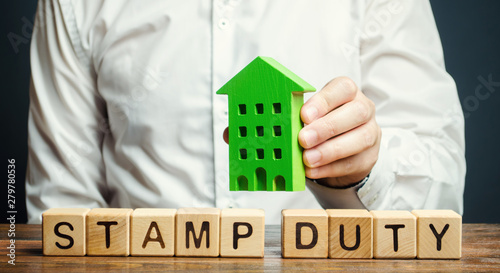 Businessman and wooden blocks with the word Stamp duty and house. Taxes assessed during the transfer of real estate between two parties. Buying housing and land. Property. Stamp Duty Land Tax/ SDLT