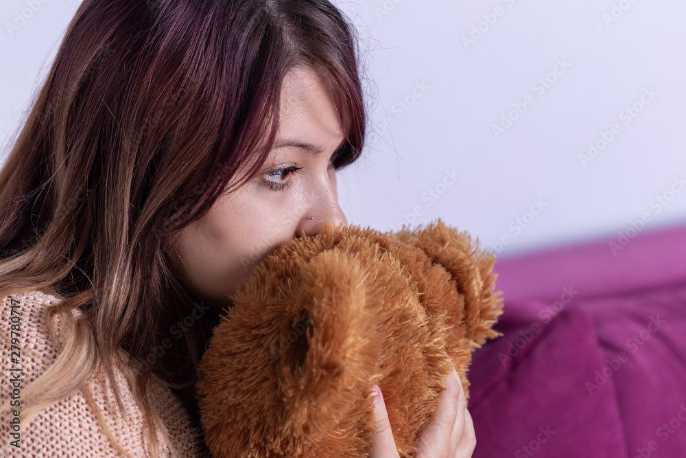 Unhappy lonely depressed woman at home, she sitting on couch and covering her face on stuffed animal, depression concept Unhappy lonely depressed woman at home, she sitting on couch and covering her face on stuffed animal, depression concept