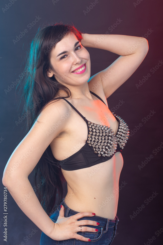 Beautiful young sexy brunette woman posing on a dark background in a riveted top on a dark background. The concept of grooming and attractiveness.