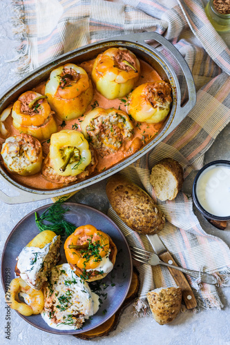 Baked bell peppers with filling. Minced rice, carrots in a plate on a wooden stand and pan and grey concrete background in traditional rustic style with appliances and bread top view