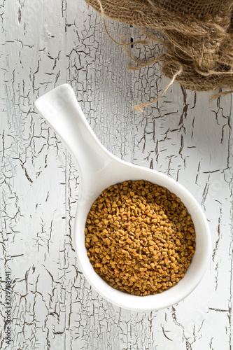 Dried, raw fenugreek seed in white bowl on white rustic wooden table background top view flat lay from above photo