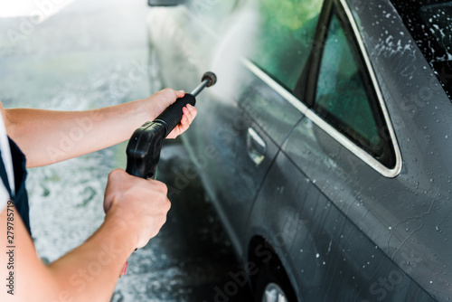cropped view of car cleaner holding pressure washer while standing near car