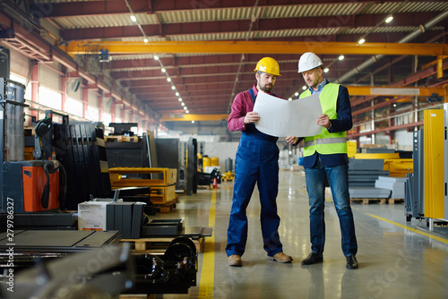 Engineers in hard hats working on a blueprint at the industrial plant.