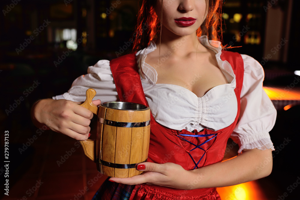 attractive young girl in traditional Bavarian clothes with a wooden mug of beer on the background of the pub during the celebration of Oktoberfest