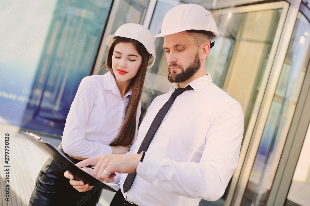 Εκτύπωση καμβά A man with a beard and a woman in business clothes is studying drawings and docu