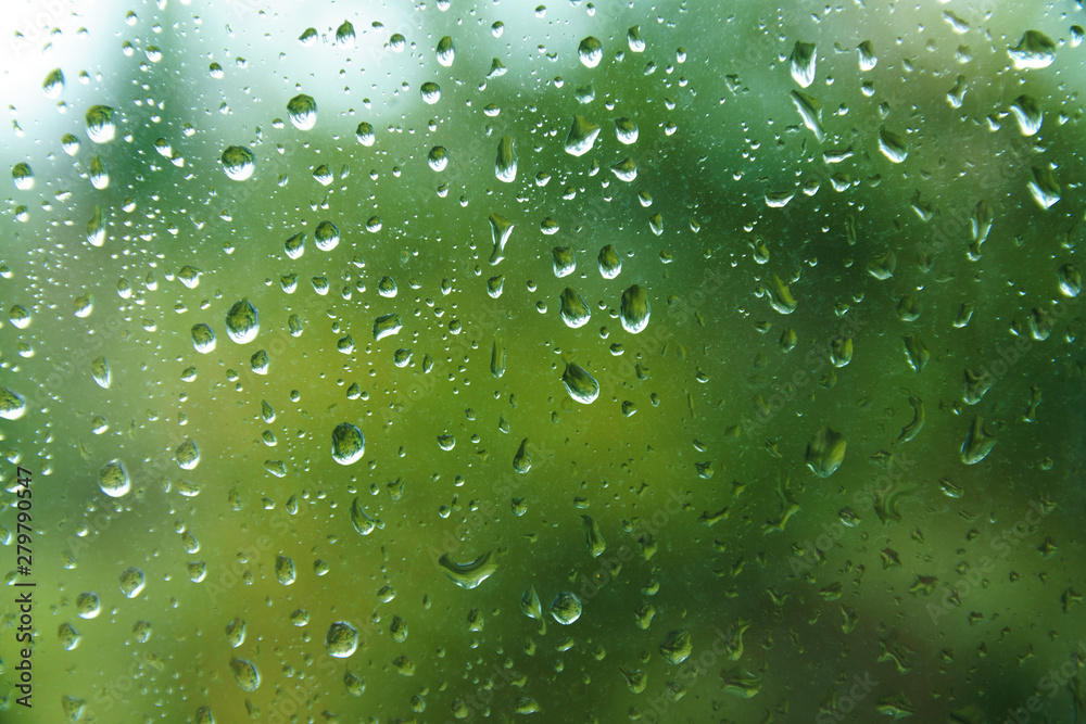 Beautiful view from window at dim outlines nature backdrop. Water drops on glass with blurred edges. View from window on rainy day. Rain drop on windowpane with blur tree background.