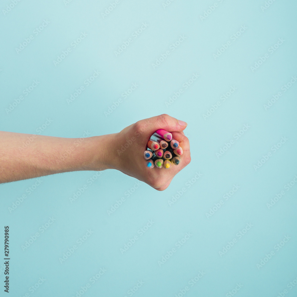Fotografie Human hand holding bunch of colorful pencils on blue backdrop