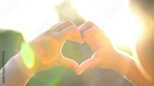 Young girl making the symbol of love over sunset