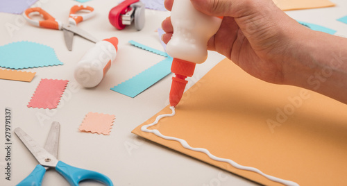 Human hand applying white glue on orange paper with scissor and stapler photo