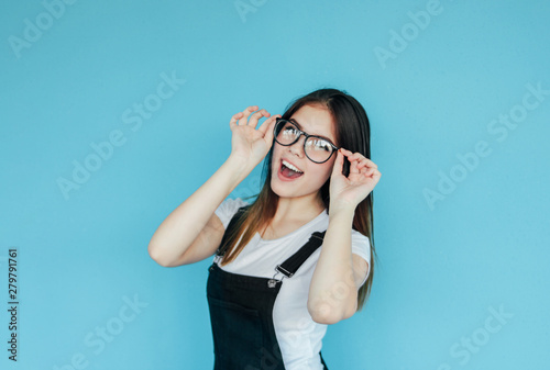 Beautiful happy girl in glasses with dark long hair in white t-shirt isolated on blue background