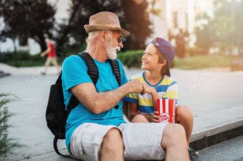 Happy grandfather enjoying with his grandson while eating popcorn outdoors in city street.