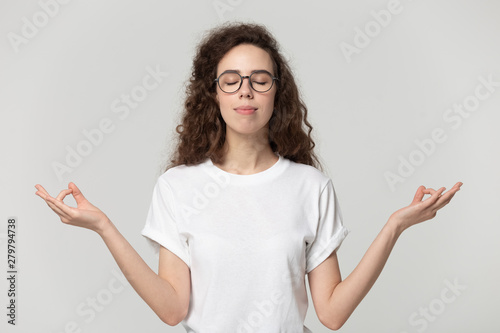 Tranquil young woman meditating pose on grey studio background
