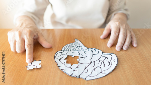 Elderly woman hands putting missing white jigsaw puzzle piece down into the place as a human brain shape. Creative idea for memory loss, dementia, Alzheimer's disease and mental health concept. photo