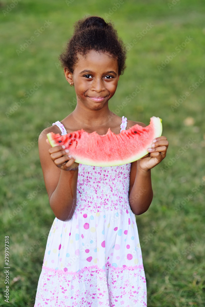 Φωτογραφία cute black African American baby girl eating juicy ripe watermelon on Park backg