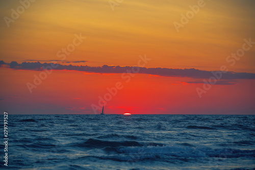 Sailboat on the horizon on the bright background of incredible sunset from the setting sun, the blue sea in the foreground © Inna