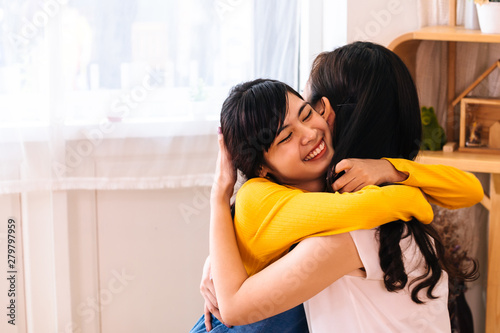 Face of smiling Asian teenage daughter and Asian middle-aged mother hugging with happy warm expression and tenderness in indoor living room at home. They have good relationship together.