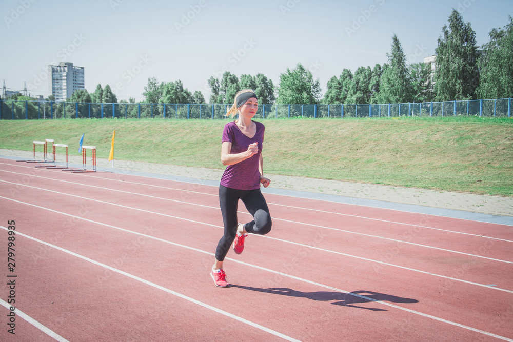 Young fitness blonde woman in shorts and top running on a stadium track