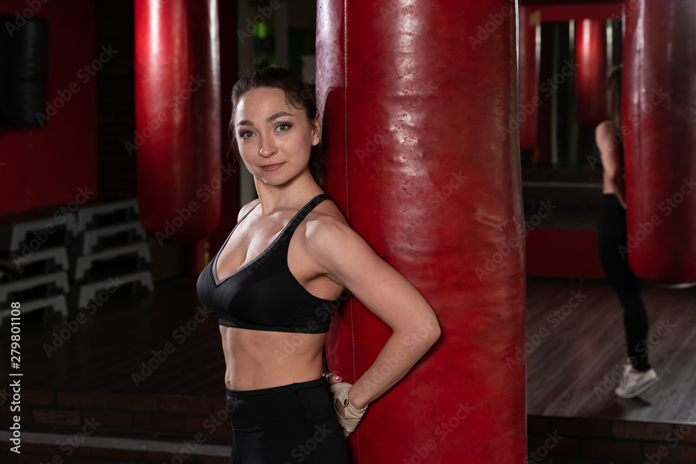 sexy fighter girl in gym with boxing bag. Long hair woman fitness model resting after boxing