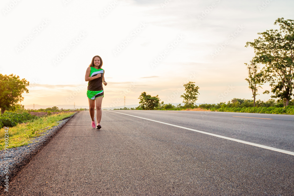 Along the road in the hillside area at the time of the sun set woman is exercising by running.