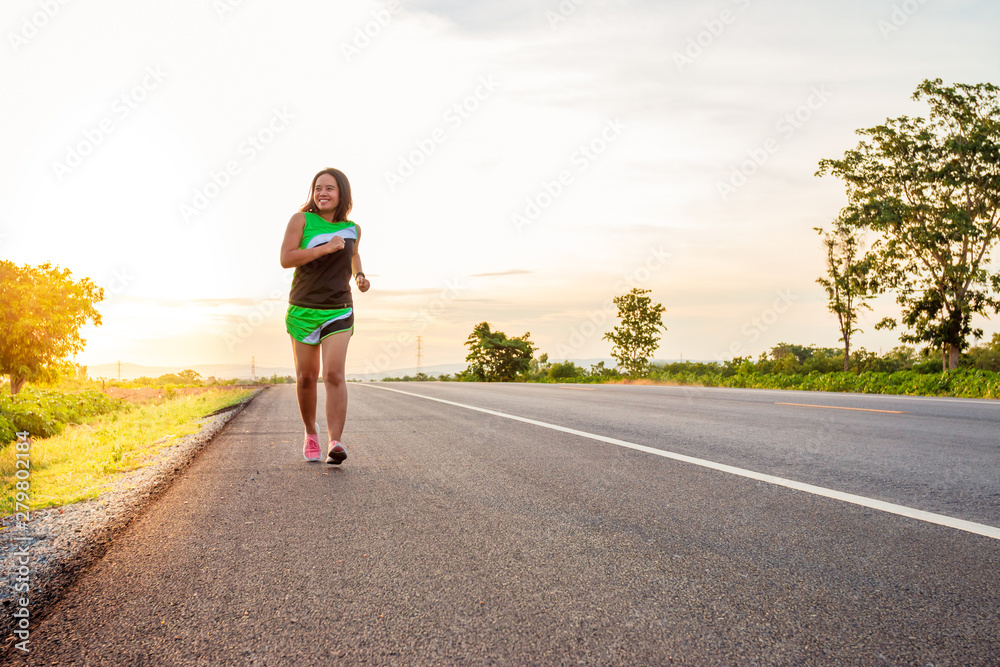 Along the road in the hillside area at the time of the sun set woman is exercising by running.