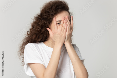 Fotografi Sly girl hiding face behind hands peeps through fingers