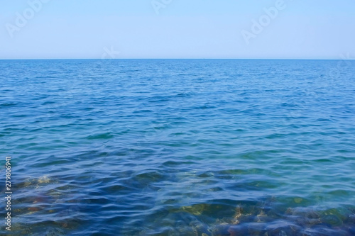 Seascape with transparent blue water, stones and clear sky at sunny day. Nature background with sea water, horizon and sky.