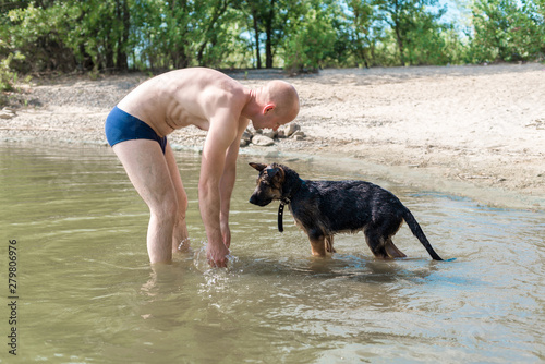 Happy German shepherd puppy playing with a man in the river on a Sunny summer day. The concept of playing with a dog in nature and walking on the beach with Pets
