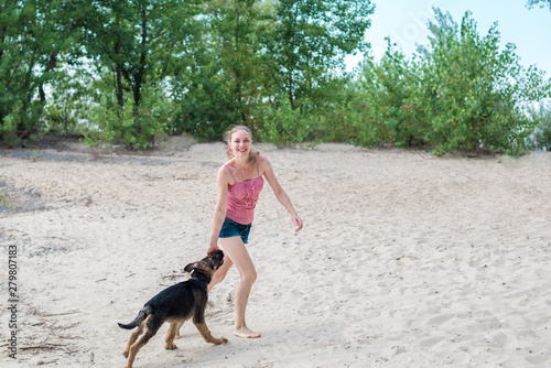 Happy German shepherd puppy and beautiful blonde girl have fun running on the beach and playing on the sand on a Sunny summer day by the river. The concept of walking and playing with a dog in nature