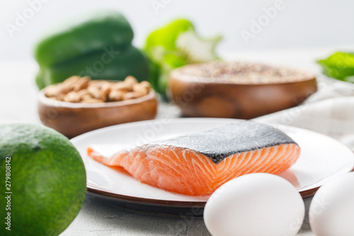 selective focus of fresh raw salmon on white plate near avocado and eggs, ketogenic diet menu