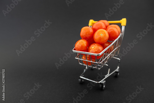 Fototapeta Naklejka Na Ścianę i Meble -  Mini shopping cart with cherry tomatoes on black background