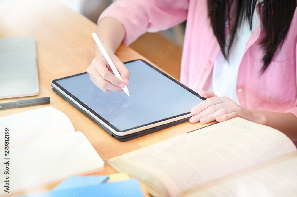 Cropped shot young woman using pen and digital tablet on wood table with books, Education concept.