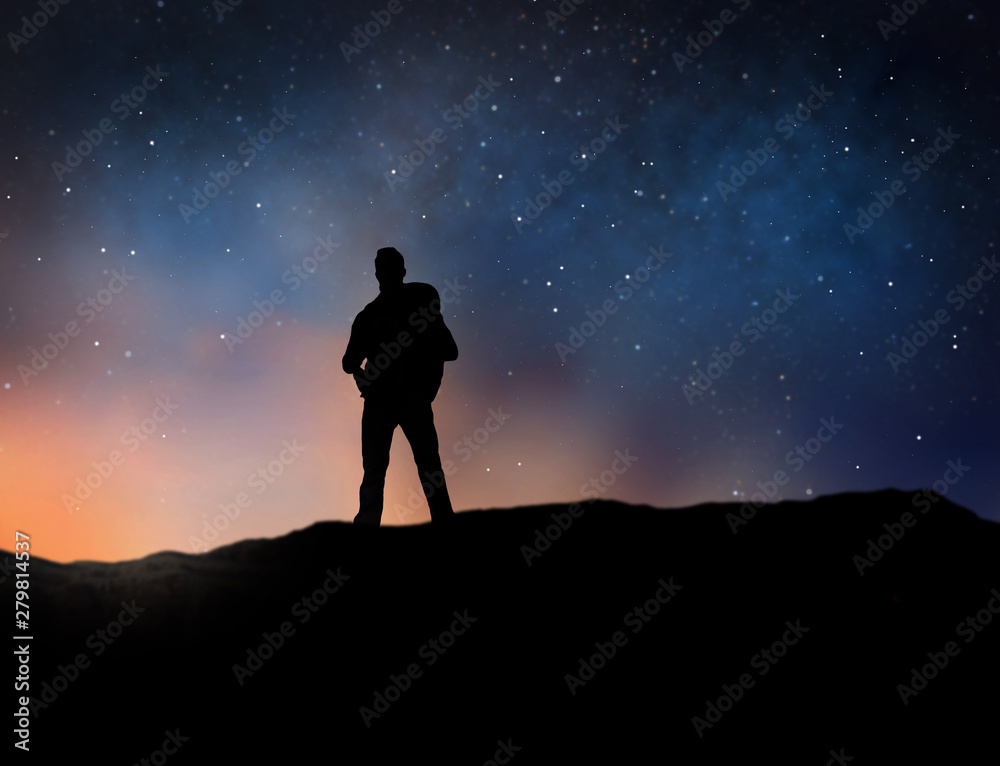 travel, tourism, hike and people concept - silhouette of traveler standing on edge of mountain over starry night sky or space background