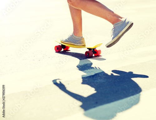 summer, extreme sport and people concept - male legs riding short modern cruiser skateboard along crosswalk