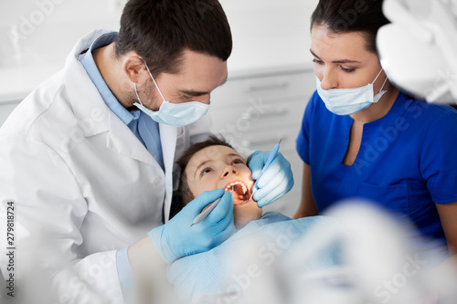 medicine  dentistry and healthcare concept - dentist with mouth mirror and probe checking for kid patient teeth at dental clinic