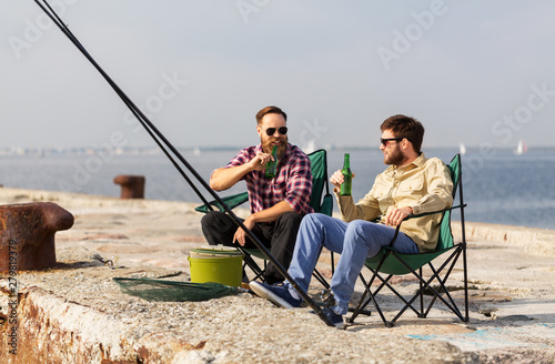 leisure and people concept - happy male friends fishing and drinking beer on pier