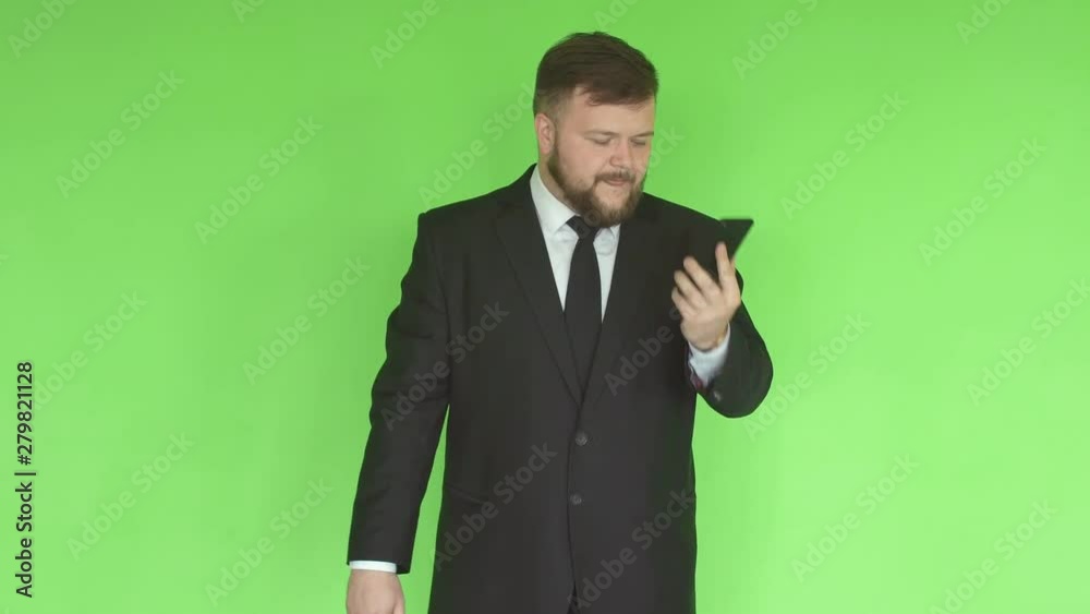 Young caucasian male businessman with a beard and in a suit twirling a hoop in the gym and talking on the phone against a green wall, healthy lifestyle