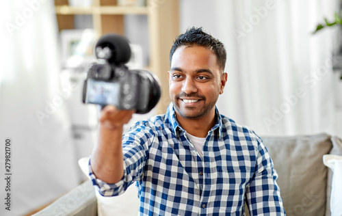 blogging, videoblog and people concept - smiling indian male video blogger with camera videoblogging at home