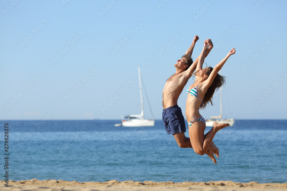 Obraz premium Excited couple jumping on the beach celebrating vacation