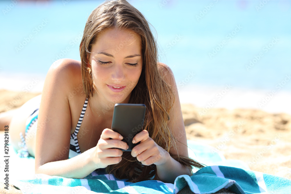 Girl in bikini sunbathing using phone on the beach