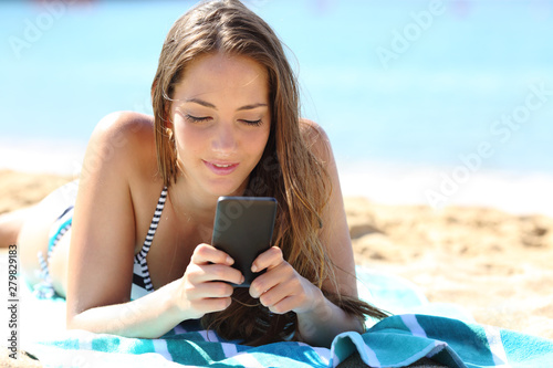 Girl in bikini sunbathing using phone on the beach